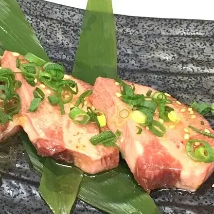 刻みねぎをのせた厚切りの牛タン塩を白い皿に盛り付けた料理写真